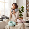 Woman enjoying comfort from Velvet Neck Pillow with additional pillows in soft colors in a cozy setting.