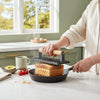 Ridged Grill Press with Wooden Handle pressing sandwich in skillet on a kitchen counter with ingredients.