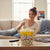 Person enjoying popcorn from a 2XL Classic Popcorn Bucket while relaxing on a couch.