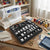 Multi-Functional Sewing Machine Presser Feet Kit displayed on a crafting table beside a sewing machine and colorful spools of thread.