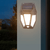 Solar Motion-Activated Wall Lamp illuminating a garden wall at night with solar panels on top.
