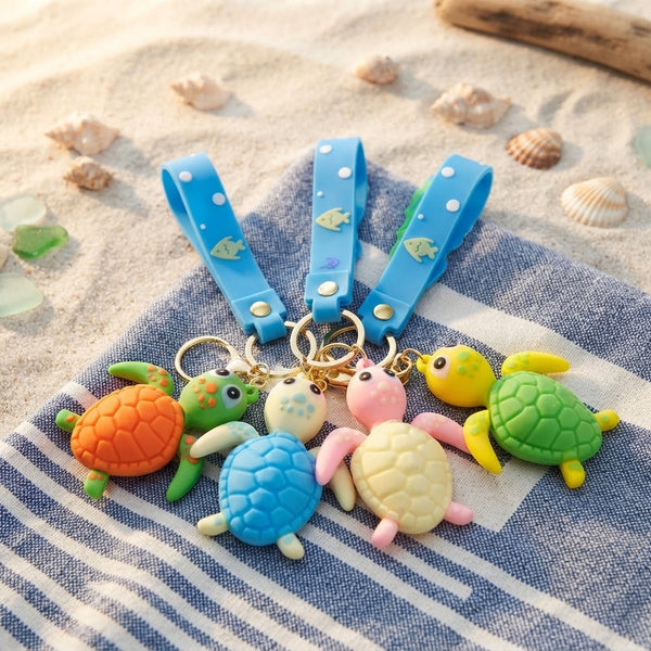 Colorful 3D Rubber Sea Turtle Keychain collection featuring vibrant turtle designs and blue straps on a sandy background.
