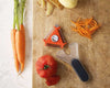 3 in 1 Peeler with Potato Eye Remover on a wooden board next to fresh carrots and tomatoes.