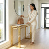 A woman placing a handbag on a Luxury Faux Marble Gold Base Console Table in a modern foyer.