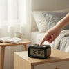 Digital Alarm Clock with Night Light on bedside table with a hand adjusting the time.