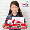 A child happily holds the Floral 15-Piece Kids Tin Tea Set with Carrying Case, featuring a teapot and cups.