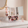 360-Degree Rotating TriFold Makeup Mirror with LED & Storage on a vanity table with cosmetics and brushes.