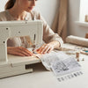 42-Piece Domestic Sewing Machine Presser Feet Set displayed while a woman sews fabric on a domestic sewing machine.