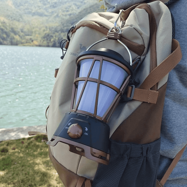 Outdoor Flicker LED Lantern attached to a backpack by a lake, providing warm ambient lighting for outdoor activities.