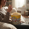 A person enjoying popcorn from an Extra Large Retro-Style Popcorn Bucket while sitting on a couch.