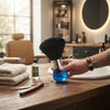 Blue and Black Barber Neck Duster Brush held over a wooden salon table with a Bay Rum bottle and grooming tools.