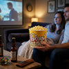 A couple enjoying a movie night with a 2XL Classic Popcorn Bucket filled with popcorn and drinks on the table.