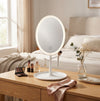 Oval LED Makeup Mirror with integrated lighting on a wooden vanity table in a cozy bedroom setting.