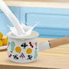 Small Enamel Milk and Butter Warming Pot with milk pouring in, surrounded by lemons on a kitchen counter.