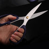Hand holding Stainless Steel Multi-Purpose Tailor Shears for fabric and paper cutting.