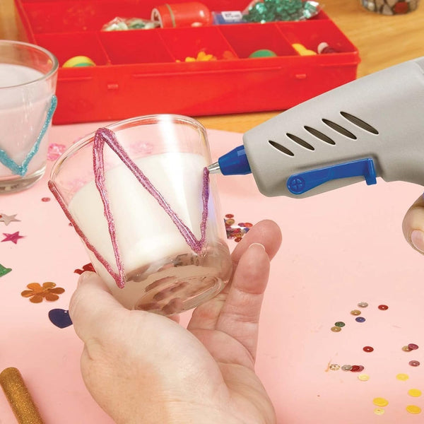 Person using a Colored Hot Glue Stick Set for DIY Crafts and Decorations to decorate a glass candle holder.