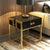 Contemporary Glam Side Pedestal featuring glossy black finish and chrome gold accents beside a sofa.