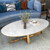Oval Faux Marble Coffee Table with Gold Metal Base elegantly displayed in a modern lounge setting.