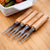 Set of 6 Stainless Steel Fruit Forks with Wooden Handles arranged on a wooden surface beside a bowl of snacks.