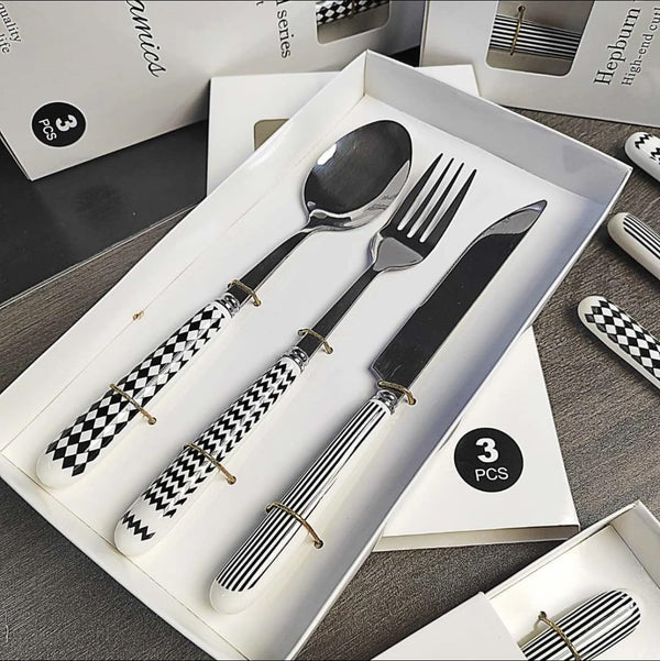Stainless Steel Cutlery Set displayed in a box featuring a spoon, fork, and knife with stylish black and white handles.