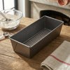 Square Nonstick Aluminum Bread Loaf Pan placed on wooden table with baking ingredients.