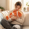 A woman hugs an Orange and White Striped Clownfish Plush Toy while sitting on a cozy couch, showcasing its vibrant colors.