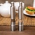Chef Master Adjustable Salt & Pepper Grinder set on a table with a tea pot and sandwich in the background.