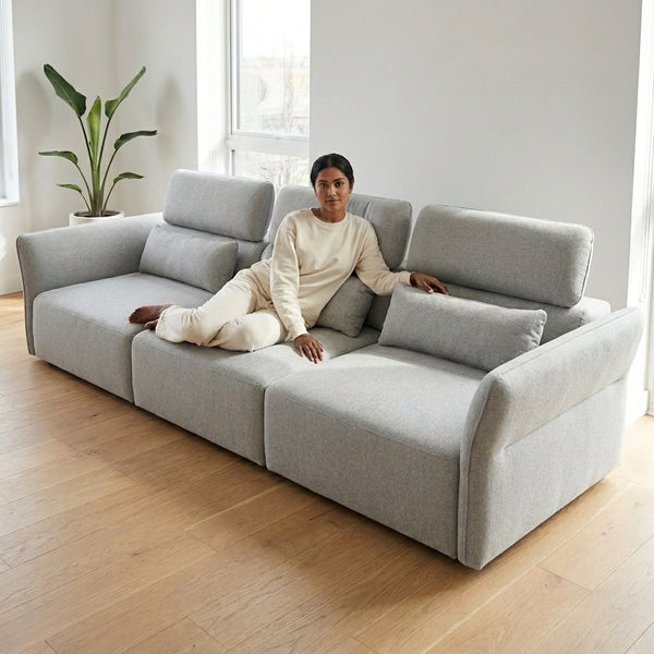 A person relaxing on the SF-622B Modular Fabric Couch with adjustable headrests in a modern living room.