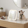 Portable Square LED Makeup Mirror on a vanity with makeup products and brushes, illuminated for easy grooming.