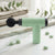 Portable Handheld Massage Gun in green color with rounded attachment, placed on a marble surface, surrounded by smooth stones.