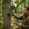 Man setting up a 4G Solar-Powered Outdoor Trail Camera on a tree in a forest.