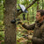 Man setting up a 4G Solar-Powered Outdoor Trail Camera on a tree in a forest.