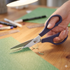 Person using Stainless Steel 6-Inch Multipurpose Scissors to cut green paper on a wooden table.