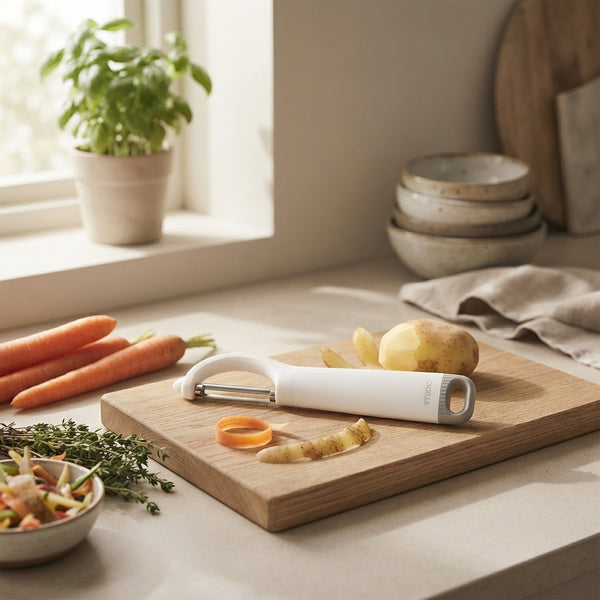 Multi-Functional Stainless Steel Vegetable Peeler on a kitchen countertop with vegetables and herbs.