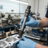 Person holding a Machined Metal Plunger Rod above mechanical equipment in a workshop.