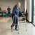 A woman using a Stainless Steel Walking Aid for support while walking in a rehabilitation center.