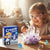 Child observing crystals with magnifying glass next to Crystal Quest Kids Growing Kit box.