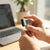 Person holding a Compact Mini Digital Camera in front of a laptop on a wooden desk.