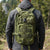 Field-Ready Multi-Pocket Backpack in green, worn by a person in a black jacket, surrounded by nature.
