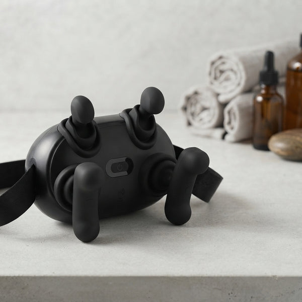 4-Head Handheld Body Massager positioned on a marble countertop with rolled towels and massage oils in the background.