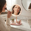 Woman using a Round Makeup Mirror with Storage Tray for her beauty routine in a bright bathroom setting.