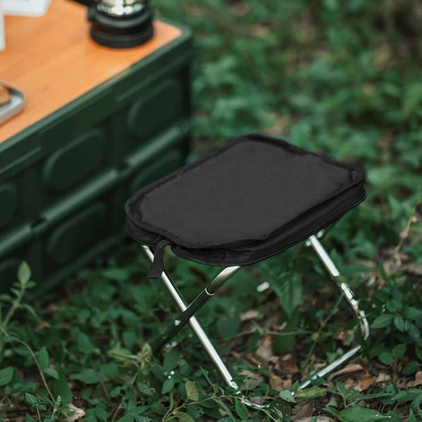 Collapsible Portable Camping Stool set up in nature beside a camping table.