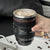 Camera Lens Travel Mug with Lid filled with iced coffee, resembling an actual camera lens.