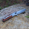 Wooden Handle Folding Tactical Pocket Knife displayed on a natural rock surface, showcasing its elegant design and sharp blade.