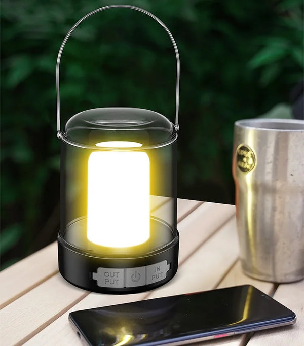 Portable USB Camping & Tent Lamp illuminating a table next to a phone and a metal cup.