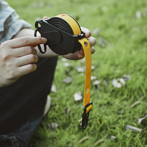 Person holding a Portable Retractable Clothes Drying Line with a yellow strap in a grassy setting.