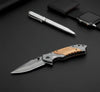 3D Pattern Blade Olive Wood Handle Pocket Knife placed on a black surface with a pen and watch.