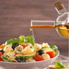 2 in 1 Olive Oil Vinegar Bottle Dispenser pouring olive oil over a fresh pasta salad garnished with vegetables.