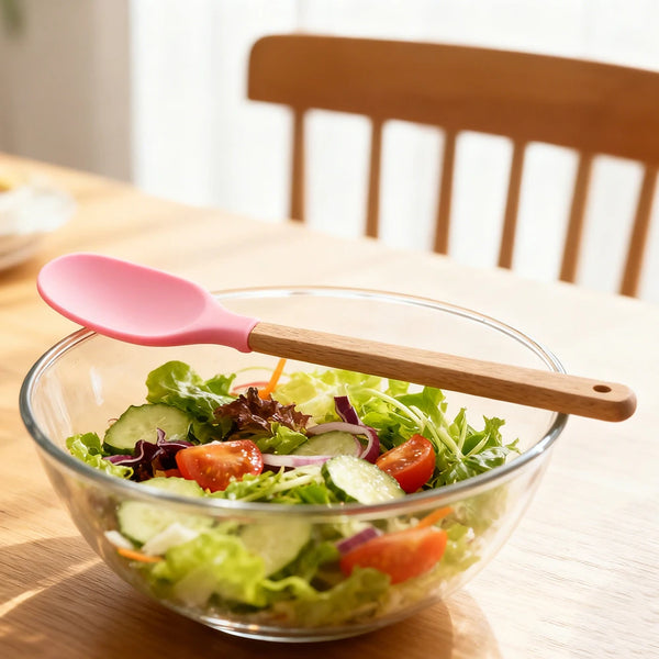 Silicone Cooking Spoon with Wooden Handle resting beside a fresh salad in a bowl on a wooden table.
