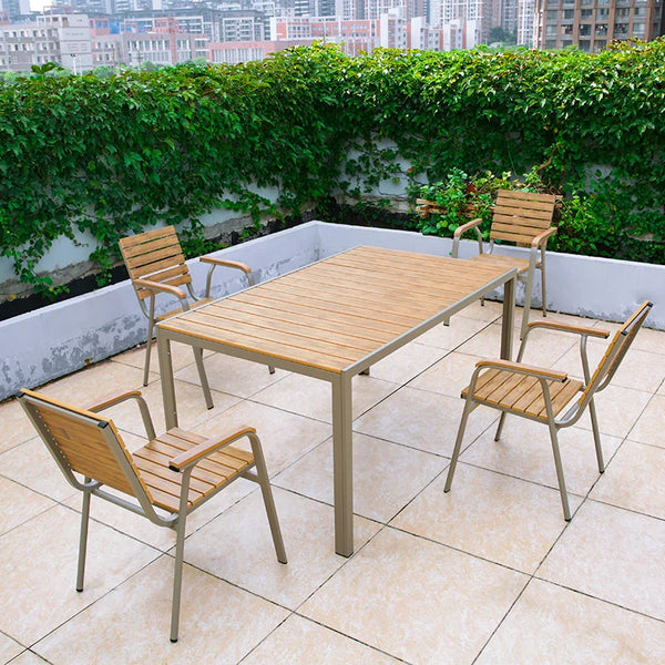 Outdoor Teak and Aluminium Dining Table with 4 Armchairs set on a patio with greenery in the background.